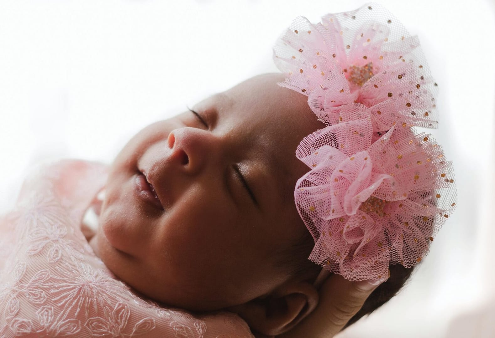 Understanding Baby Sleep Cycles: A Comprehensive Guide for Parents 1 Understanding Baby Sleep Cycles: A sleeping baby with a pink floral headband, gently cradled in a hand, wearing a pink embroidered outfit.
