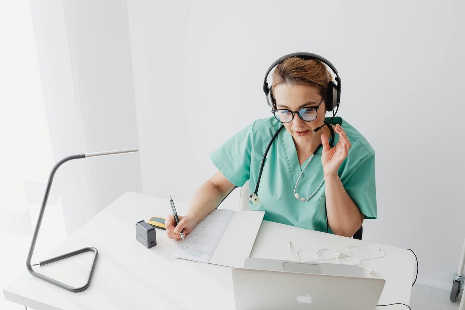Understanding Newborn Birth Weight: What's Normal & Why It Matters 3 A healthcare professional wearing scrubs and a stethoscope is sitting at a desk, using a laptop and a headset, while taking notes on a clipboard.