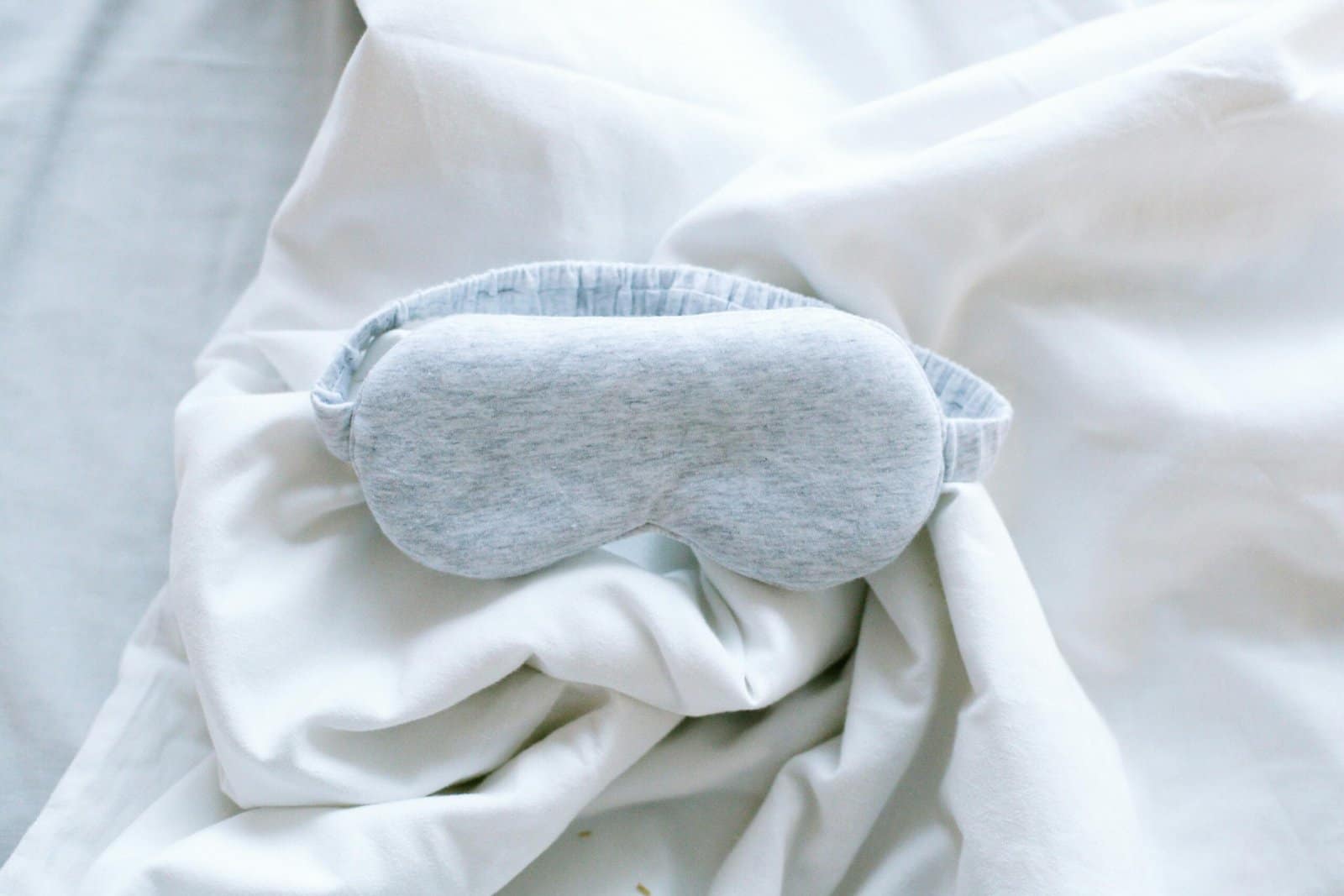 The Ultimate New Baby Hospital Bag Checklist 4 A soft grey sleep mask resting on rumpled white bed sheets.